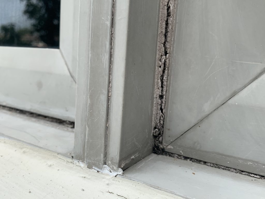 Old cracked window caulking with cracks, causing this window to leak and cause wood rot.